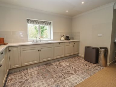 A kitchen with patterned floor tiles white cabinets a window above a sink a kettle and coffee machine on the counter and two trash bins at Millpond Bothy Woolhope