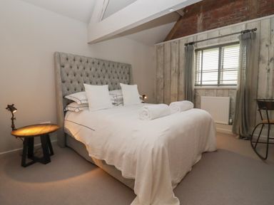A bedroom with a bed white linens bedside table lamp window and chair at Millpond Bothy in Woolhope