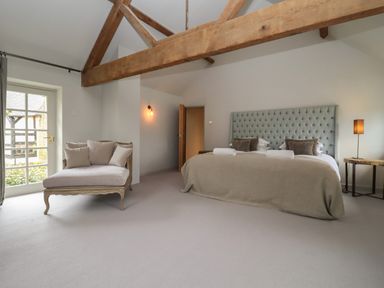 A bedroom with a bed a cushioned chair exposed wooden beams and a lamp at Millpond Bothy in Woolhope