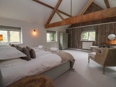 A bedroom with a bed with pillows and towels wooden beams windows a wicker chair and a dressing table at Millpond Bothy in Woolhope