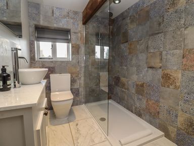 A bathroom with patterned tiled walls a glass shower enclosure a toilet and a sink on a countertop at Millpond Bothy in Woolhope