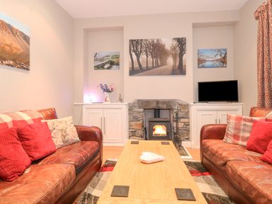 A living room with two leather sofas a wooden coffee table a stone fireplace a TV and framed pictures on the wall at Myrtle Cottage in Windermere