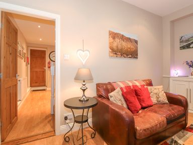 A living room with a leather sofa and red cushions a side table with a lamp and a hallway with wooden doors at Myrtle Cottage in Windermere