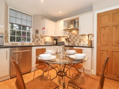 A kitchen with a glass dining table set with bowls and glasses at Myrtle Cottage in Windermere