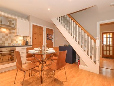 A kitchen and dining area with a glass table and four wooden chairs beneath a staircase at Myrtle Cottage in Windermere