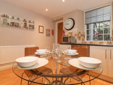 A kitchen dining area with a glass table set for four and a microwave on the counter at Myrtle Cottage in Windermere