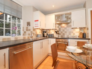 A kitchen with white cabinets stainless steel oven and dishwasher a glass dining table with wooden chairs at Myrtle Cottage in Windermere