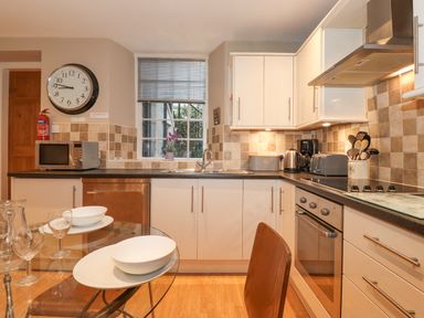 A kitchen with white cabinets a glass dining table with wooden chairs and kitchen appliances at Myrtle Cottage in Windermere