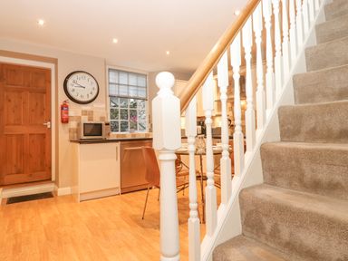 A kitchen area with a wooden door clock microwave window and stairs with carpet at Myrtle Cottage in Windermere