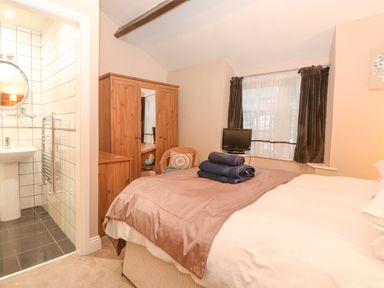 A bedroom with a bed and folded towels a wooden wardrobe and a small bathroom at Myrtle Cottage in Windermere