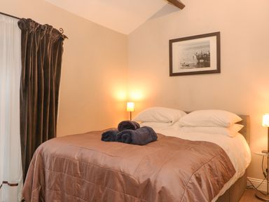 A bedroom with a bed with brown bedding and white pillows with towels on top and lamps on each side at Myrtle Cottage in Windermere