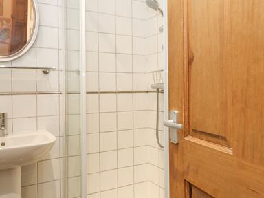 A bathroom with a white sink a shower with white tiles and a wooden door at Myrtle Cottage in Windermere