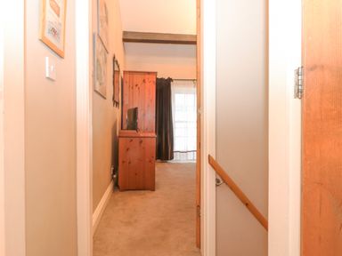A hallway with a wooden cabinet and television at the end and a staircase to the right at Myrtle Cottage in Windermere