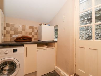 A laundry room with a washing machine countertop small fridge and a door with glass panels at Myrtle Cottage in Windermere