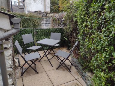 An outdoor patio area with four chairs and a square table surrounded by stone walls and greenery at Myrtle Cottage in Windermere
