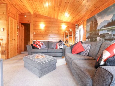 A living room with two grey sofas an ottoman and wood paneled walls at Hayeswater Lodge Burnside Park near Keswick