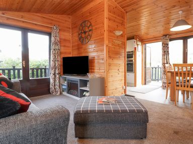 A living room with a sofa ottoman TV and dining table at Hayeswater Lodge in Burnside Park near Keswick