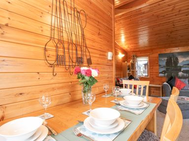 A dining table set with plates bowls glasses and a vase of flowers in a wooden interior at Hayeswater Lodge Burnside Park near Keswick