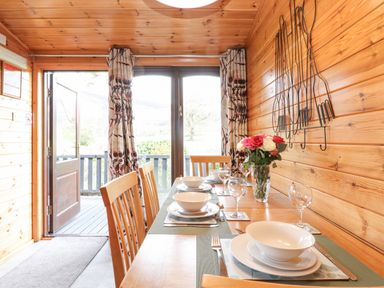 A dining table set with plates bowls glasses and cutlery in a wooden room with open doors at Hayeswater Lodge Burnside Park near Keswick