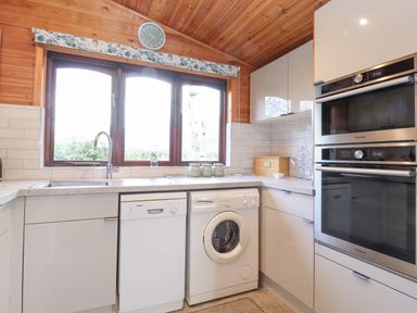 A kitchen with a window above a countertop a sink dishwasher washing machine and stacked ovens at Hayeswater Lodge Burnside Park near Keswick