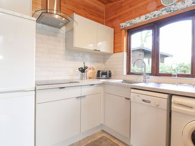 A kitchen with white cabinets a refrigerator a toaster a dishwasher a washing machine and a window at Hayeswater Lodge Burnside Park near Keswick
