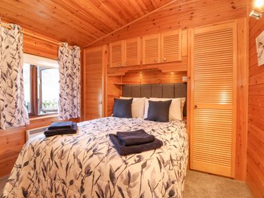 A bedroom with a double bed white and blue patterned bedding blue pillows wooden wardrobes and a window with patterned curtains at Hayeswater Lodge Burnside Park near Keswick