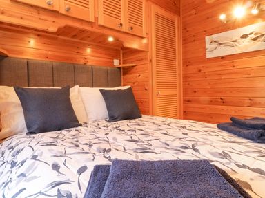 A bedroom with a bed featuring patterned bedding and dark pillows with wooden wall panels at Hayeswater Lodge Burnside Park near Keswick