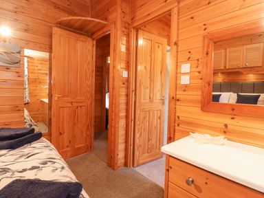 A wooden bedroom with an open door and a dresser with a mirror at Hayeswater Lodge Burnside Park near Keswick