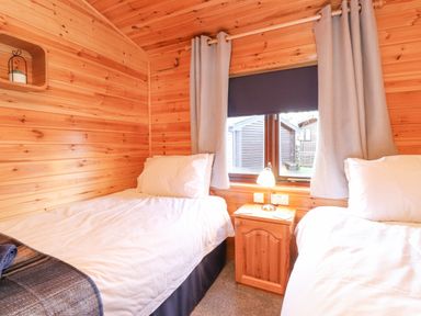 A bedroom with two single beds a wooden nightstand lamp and a window with curtains at Hayeswater Lodge Burnside Park near Keswick