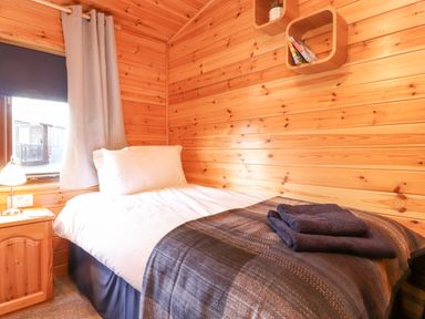 A bedroom with a single bed a wooden nightstand and wall shelves at Hayeswater Lodge Burnside Park near Keswick