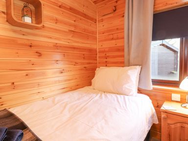 A small bedroom with wooden walls a single bed and a window with curtains at Hayeswater Lodge Burnside Park near Keswick