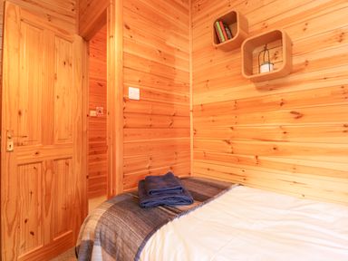 A bedroom with wooden walls a bed with blue towels and shelves with books and a plant at Hayeswater Lodge Burnside Park near Keswick