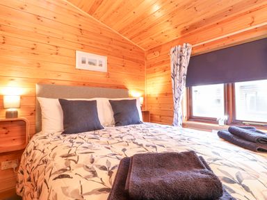A bedroom with a bed covered by a patterned duvet and pillows next to a window with curtains and blinds at Hayeswater Lodge Burnside Park near Keswick