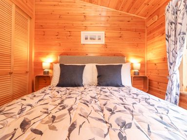 A bedroom with a double bed with patterned bedding two pillows two bedside tables with lamps and wooden walls and ceiling at Hayeswater Lodge Burnside Park near Keswick