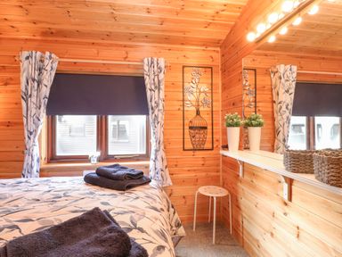 A bedroom with floral curtains towels on bed and a stool in Hayeswater Lodge Burnside Park near Keswick