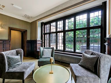 A sitting area with two sofas and an armchair around a round table near large windows in a room at Tudor Grange in Bournemouth