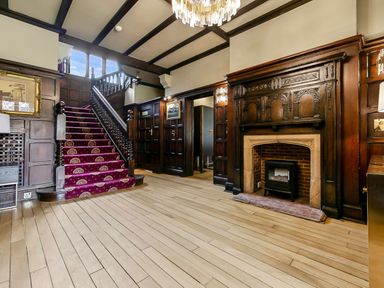 A hallway with wooden staircase covered by red carpet and a wooden fireplace at Tudor Grange in Bournemouth