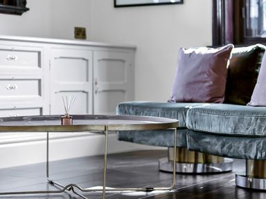 A living room with a round metal coffee table and a velvet sofa with cushions at Tudor Grange in Bournemouth