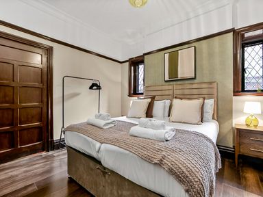 A bedroom with a double bed with pillows and towels two windows a wooden door and a lamp on a bedside table at Tudor Grange in Bournemouth