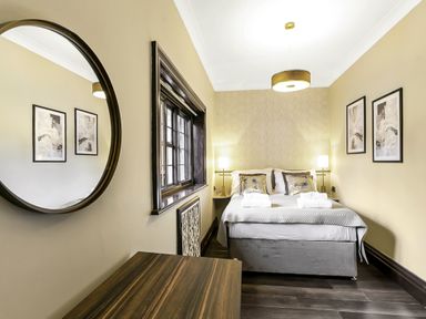 A bedroom with a bed two bedside lamps two framed pictures a round mirror and a wooden desk at Tudor Grange in Bournemouth