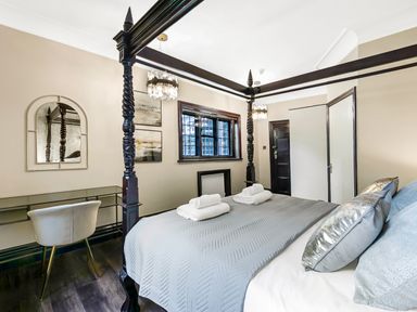 A bedroom with a four poster bed a desk with a chair and a window at Tudor Grange in Bournemouth