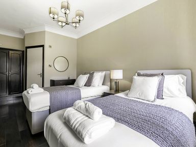 A bedroom with two single beds bedside table with lamp dresser with round mirror at Tudor Grange in Bournemouth