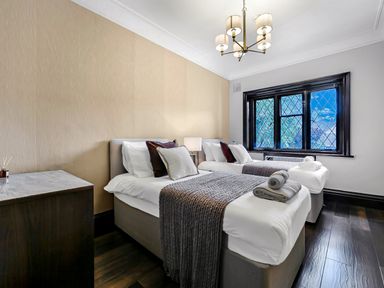 A bedroom with two single beds bedside table lamp and a window at Tudor Grange in Bournemouth