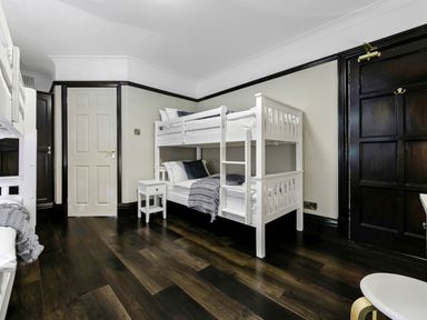 A bedroom with two white bunk beds a small white bedside table and dark wooden doors at Tudor Grange in Bournemouth