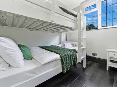 A bedroom with white bunk beds green blanket and pillows next to a window at Tudor Grange in Bournemouth