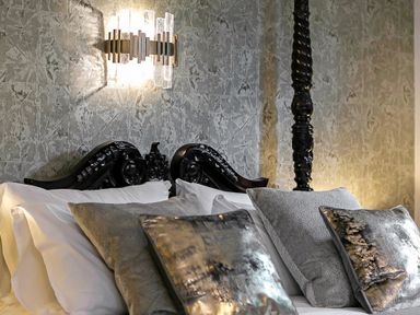 A bed with carved wooden headboard and multiple cushions under a wall-mounted light at Tudor Grange in Bournemouth