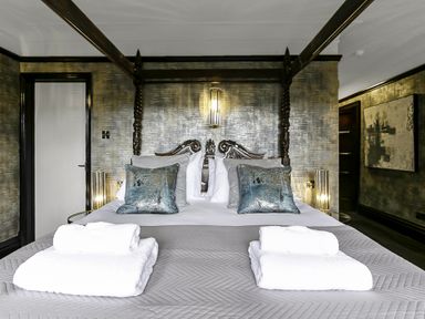 A bedroom with a four-poster bed pillows folded towels and bedside lamps at Tudor Grange in Bournemouth