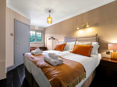 A bedroom with a double bed with orange pillows and blankets bedside tables lamps and a window at Tudor Grange in Bournemouth