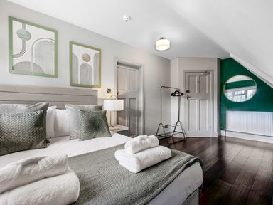 A bedroom with a bed with pillows and folded towels a lamp two doors a clothing rack and a round mirror on a green wall at Tudor Grange in Bournemouth