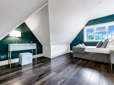 A bedroom with a bed beside a window and a desk with a lamp and stool under a sloped ceiling at Tudor Grange in Bournemouth